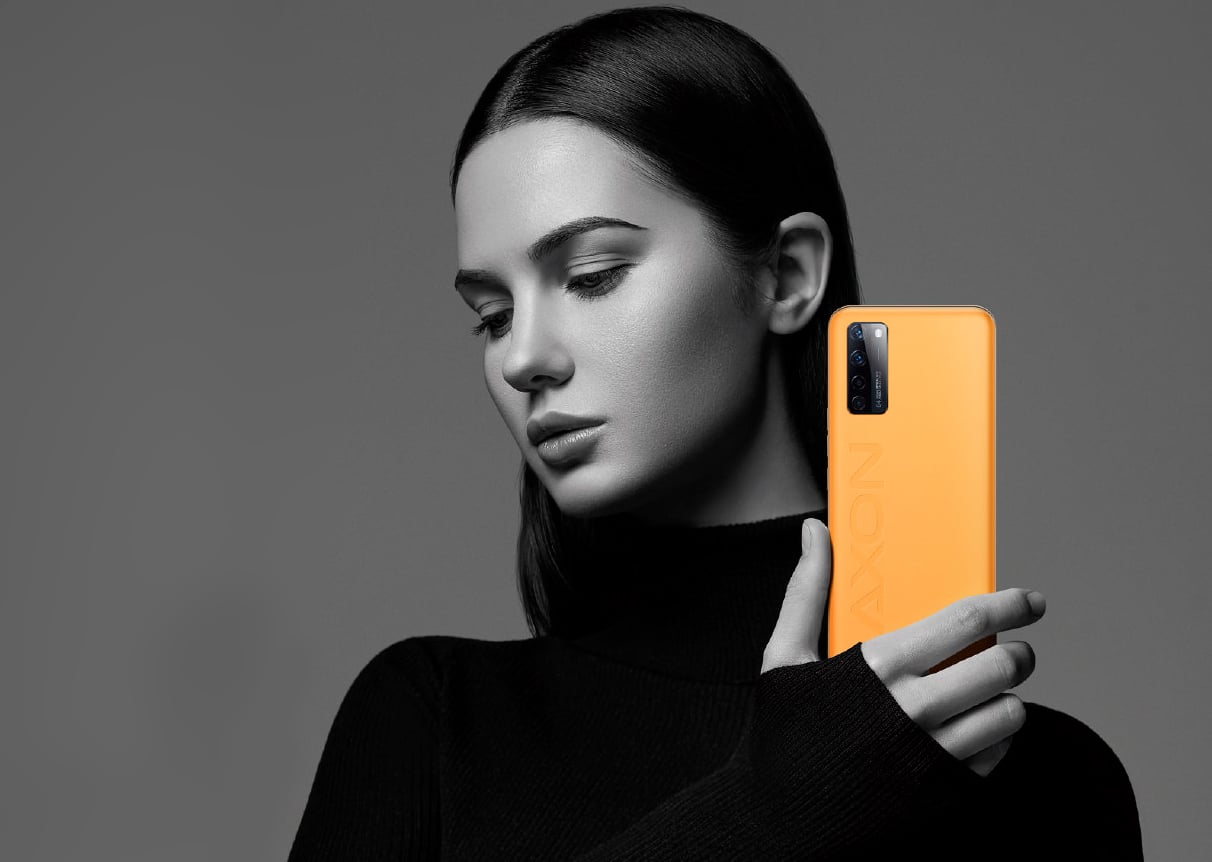 imagem de fundo acinzentado, com uma modelo branca de casaco preto, segurando o axon 20 extreme com a parte traseira virada