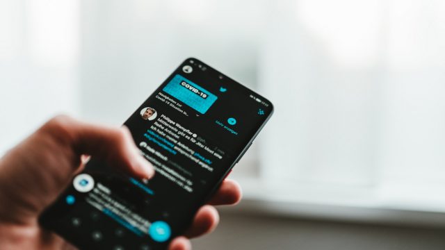 celular rodando twitter em modo noturno e fundo desfocado