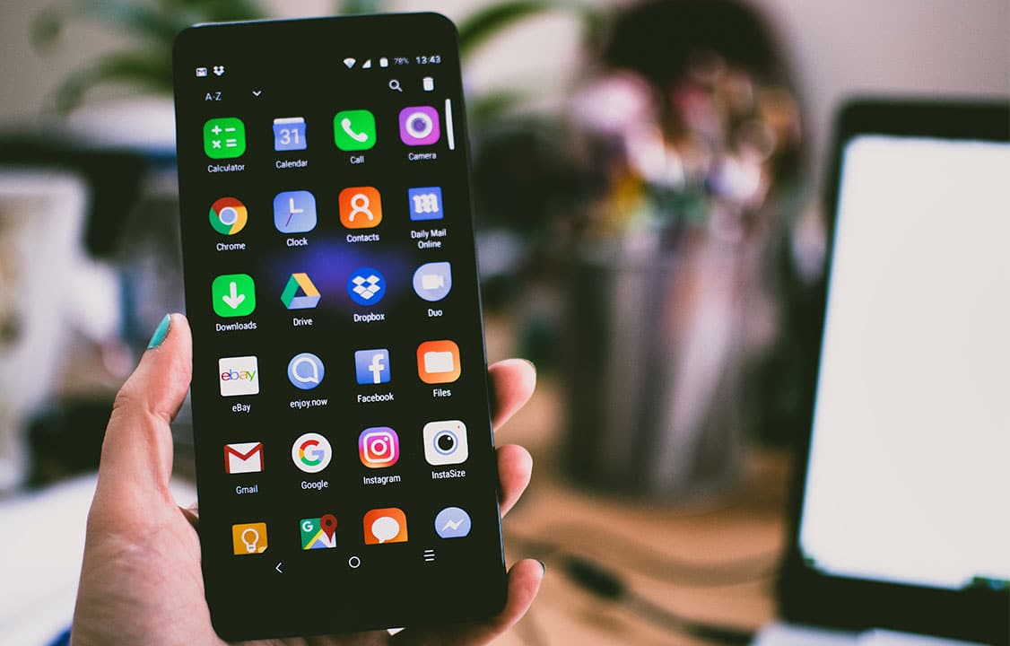 Nova versão do Google Files virá com recurso que salva fotos apagadas - imagem mostra uma mão segurando um celular android em um escritório