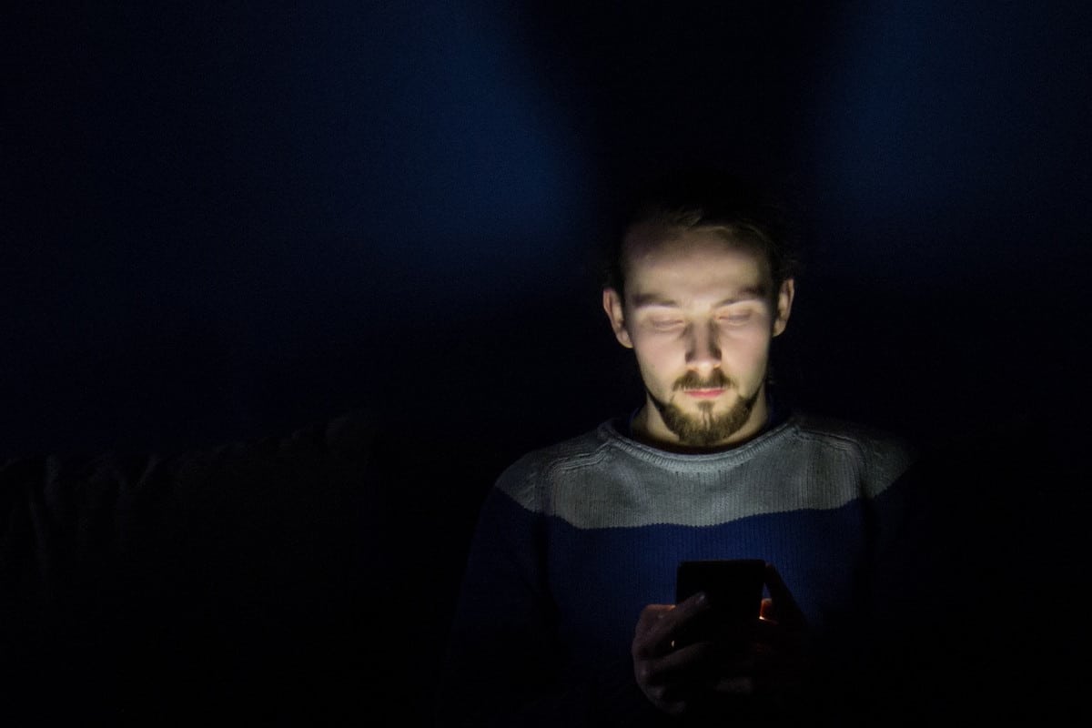 Imagem de rapaz usando smartphone no escuro