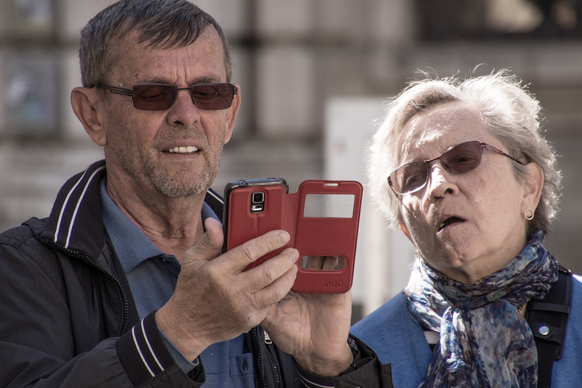 casal de idosos com óculos escuros utilizando um aparelho celular com capa vermelha