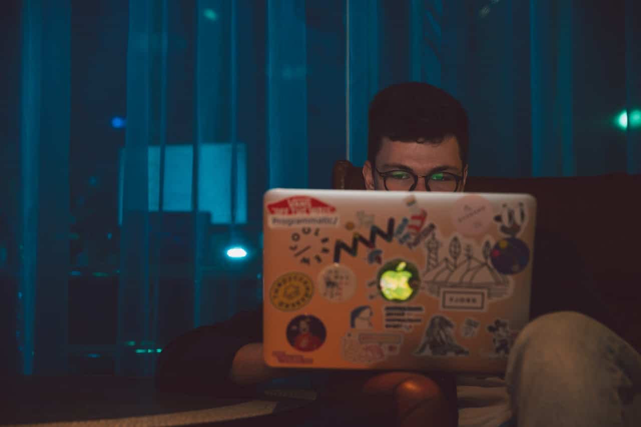 jovem,a meia luz, jogando vídeo game em laptop da Apple