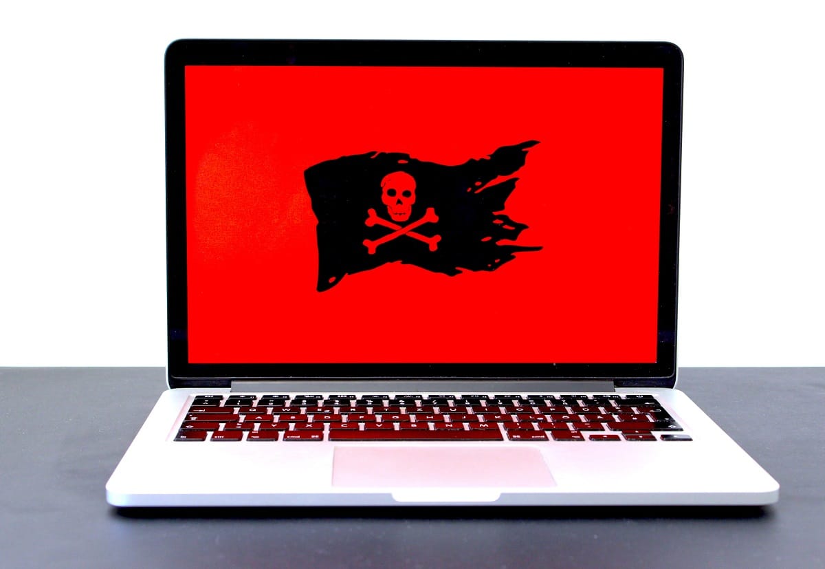 Laptop mostrando uma tela vermelha com bandeira de pirata, indicando presença de malwares ou spywares