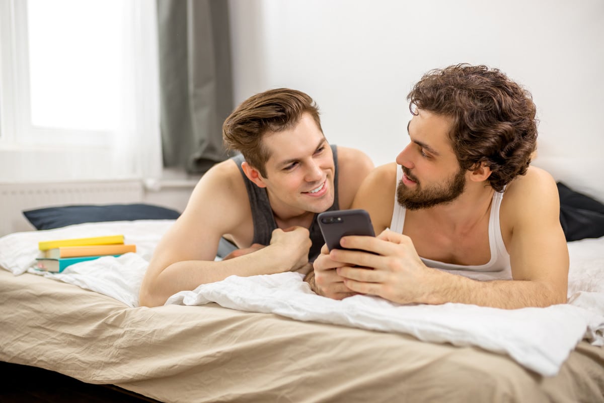 Imagem de casal gay na cama para matéria sobre Grindr compartilhar informações dos usuários