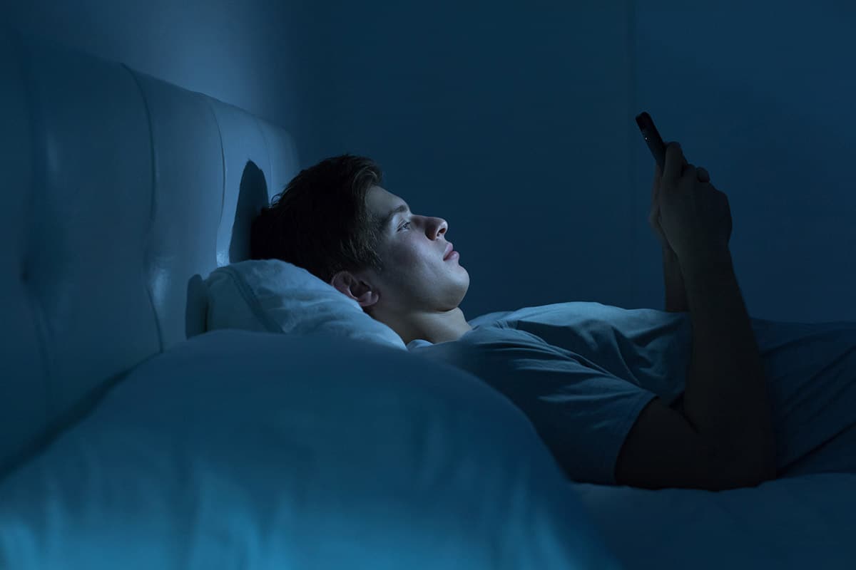 homem deitado na cama olhando celular