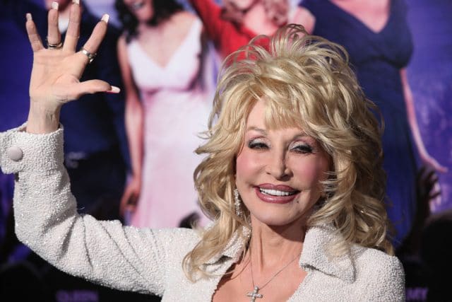 Imagem de Dolly Parton, cantora de country americano, acenando como referência da campanha de 5 meses grátis da Apple Music