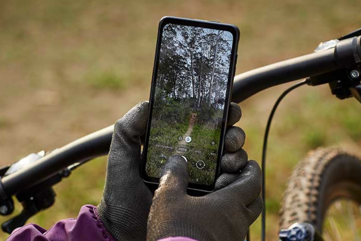 Homem com luvas segura um celular resistente enquanto monta uma bicicleta