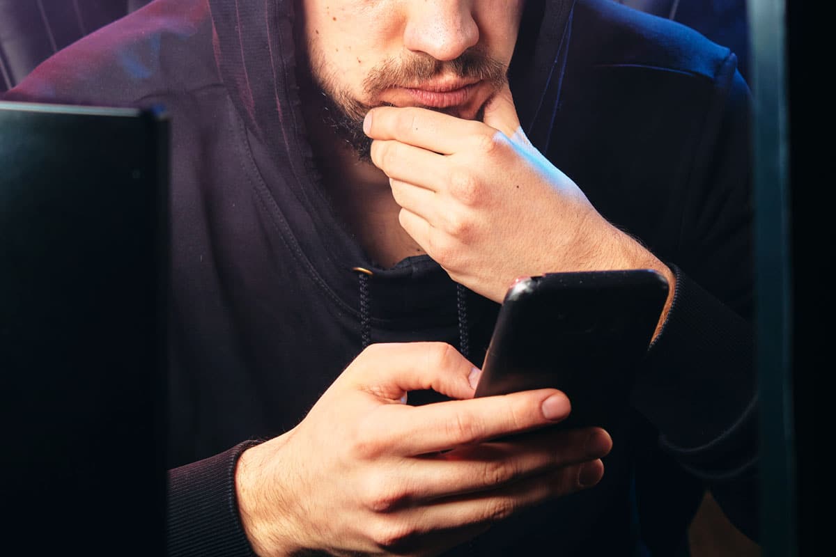 hacker olhando para celular na frente do pc