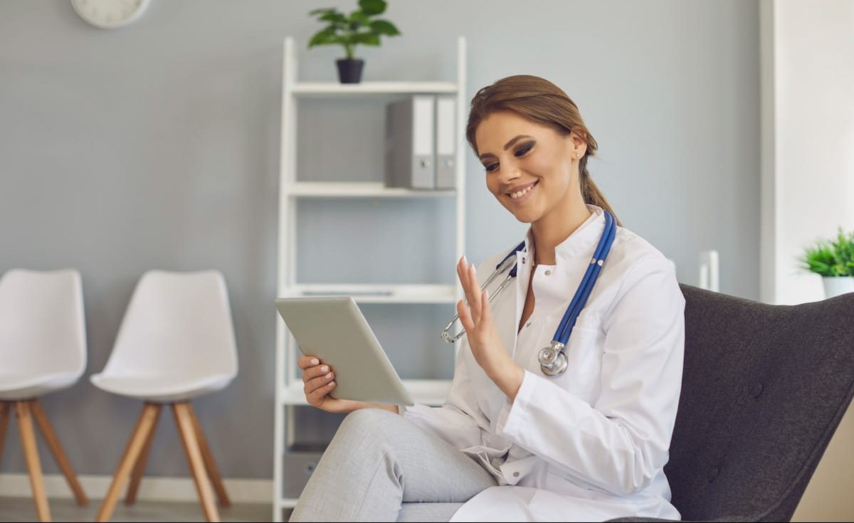 médica acenando para cliente em tablet dentro de consultório