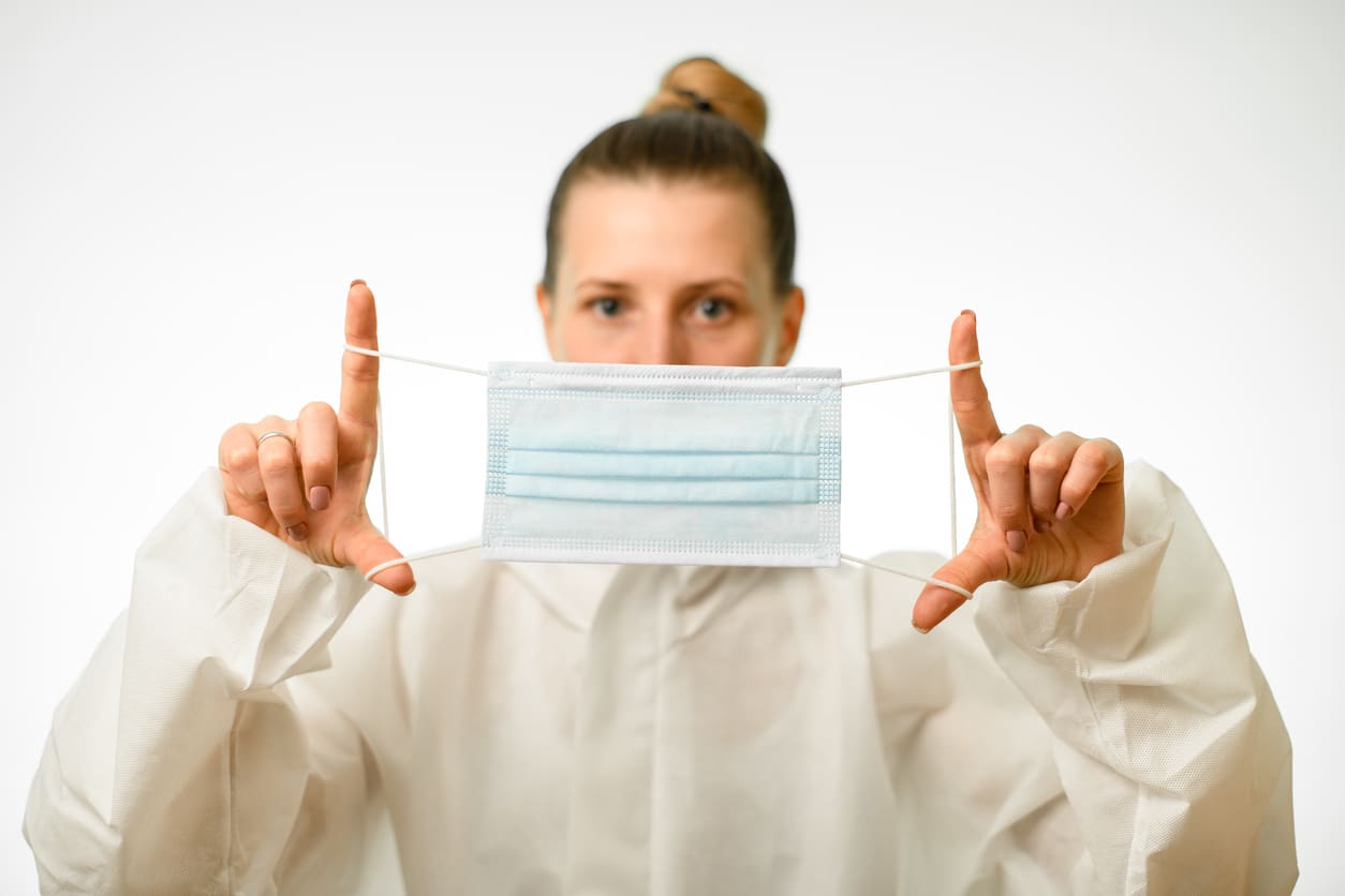 mulher de branco segurando uma máscara de procedimento médico de frente para seu rosto