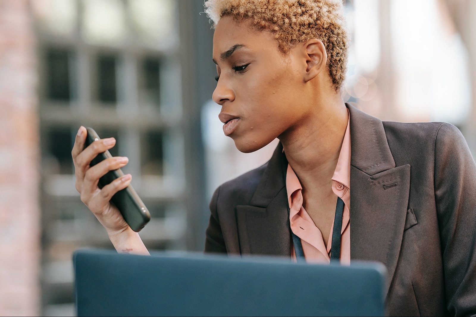 Mulher negra olha para celular na frente de um notebook