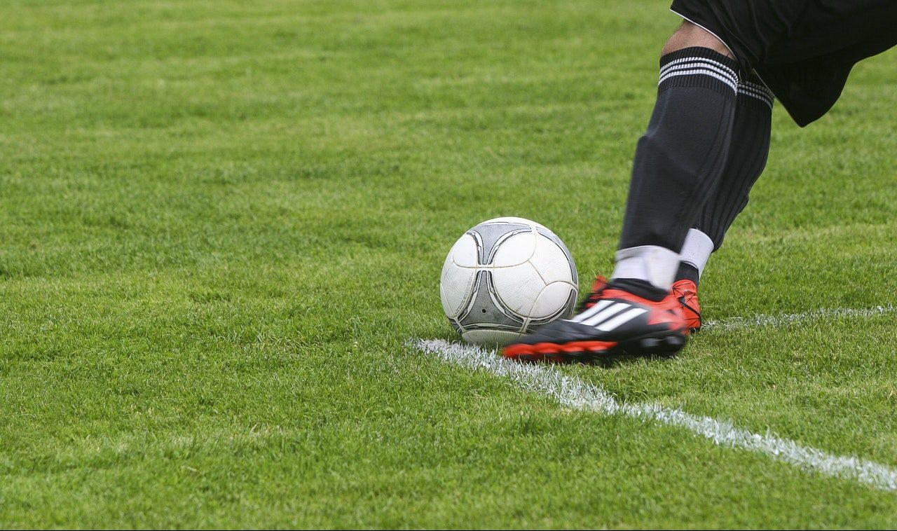 Perna chutando bola em campo de futebol