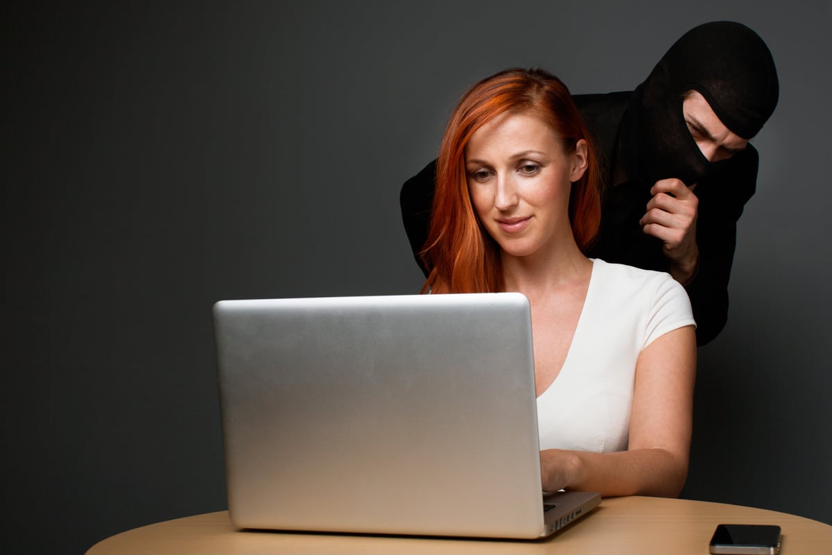 mulher usando notebook sem reparar em ladrão que espia