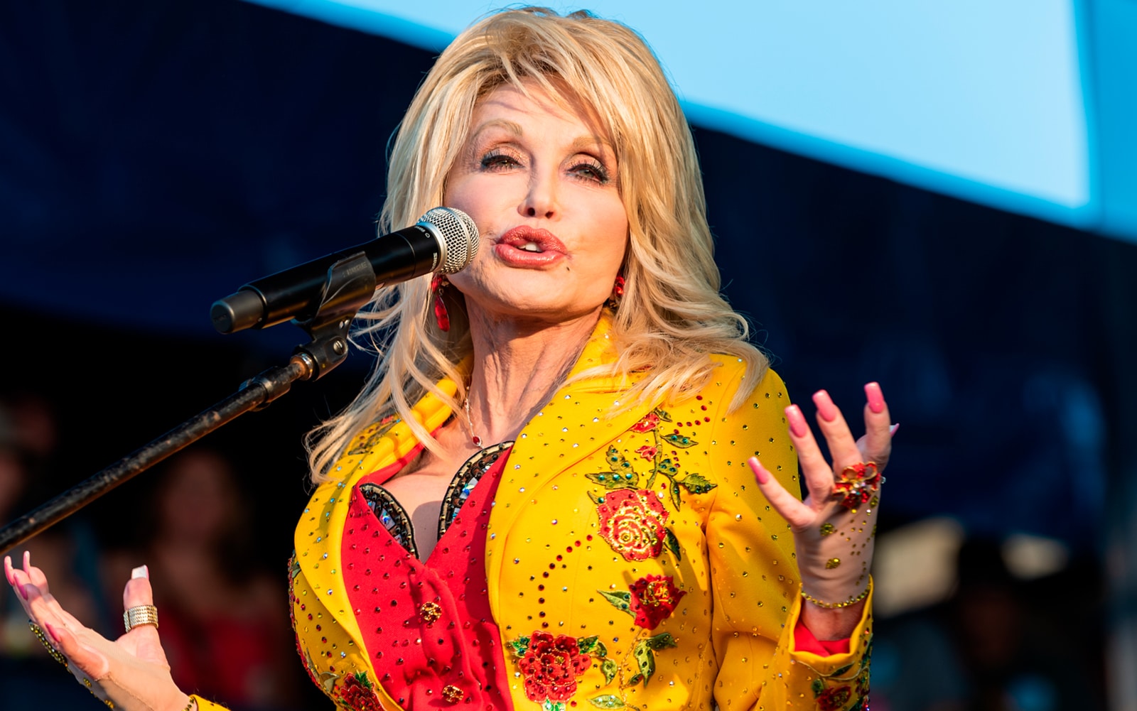 Imagem de Dolly Parton, cantora de country americano, acenando como referência da campanha de 5 meses grátis da Apple Music