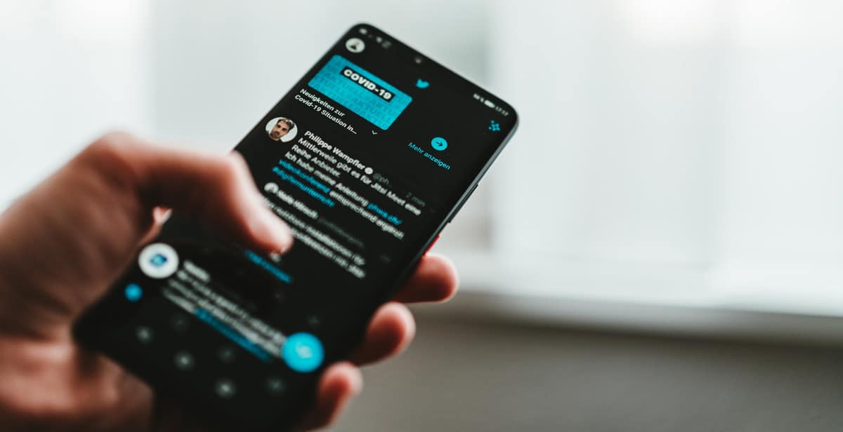 homem segurando celular com twitter aberto em modo noturno