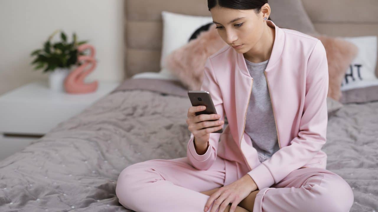 Imagem de uma mulher sentada na cama decidindo se baixa Telegram ou Whatsapp