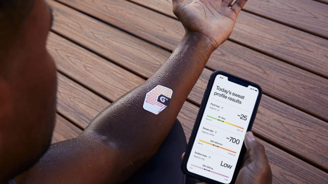 Braço esquerdo com o patch de suor da Gatorade. Há também celular iPhone com o Gx App exibindo as informações de suor