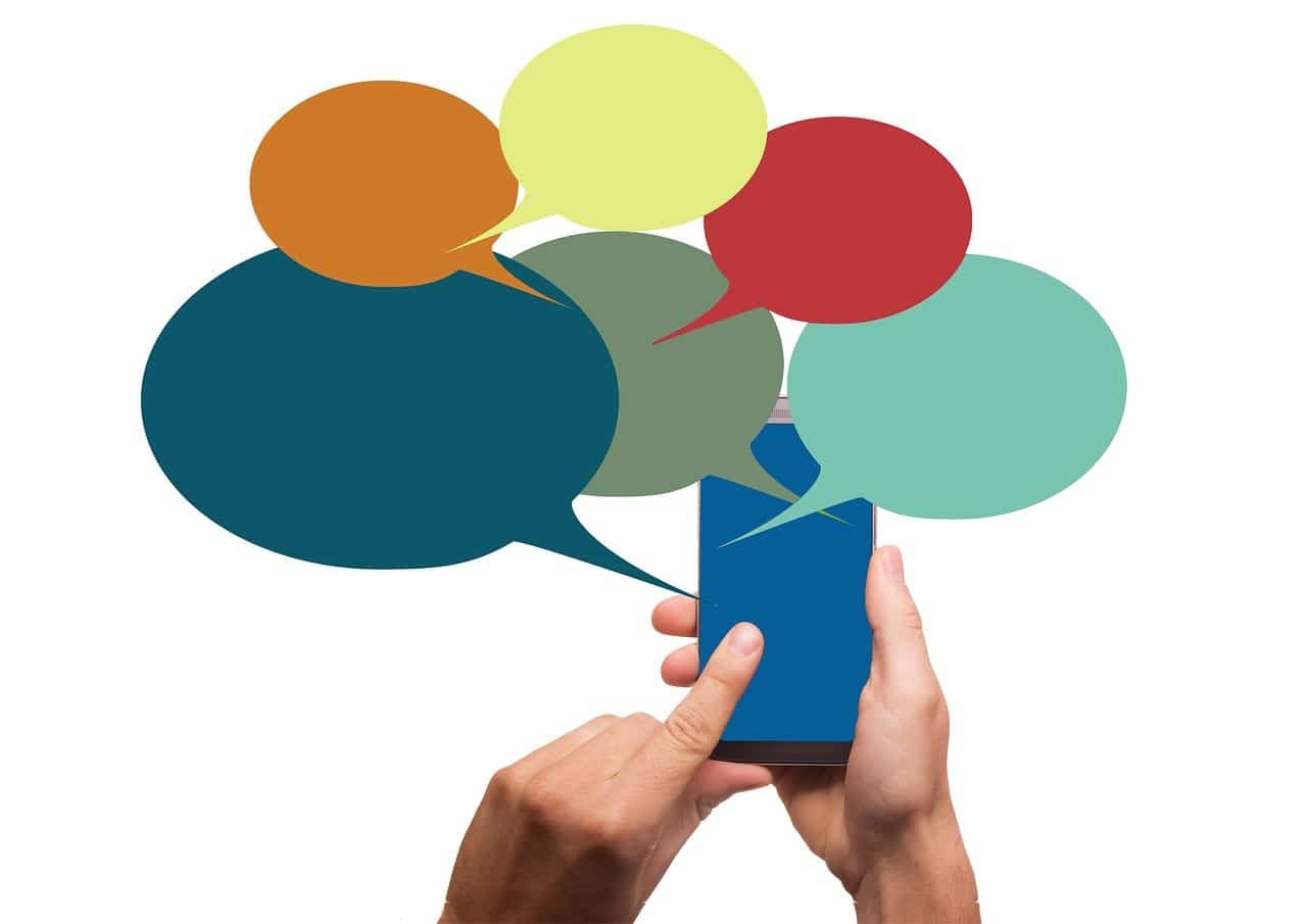Imagem mostra mãos segurando um celular e balõezinhos de conversa saindo do aparelho, para simbolizar um chat em grupo, recurso que o TikTok quer implementar ainda em 2021