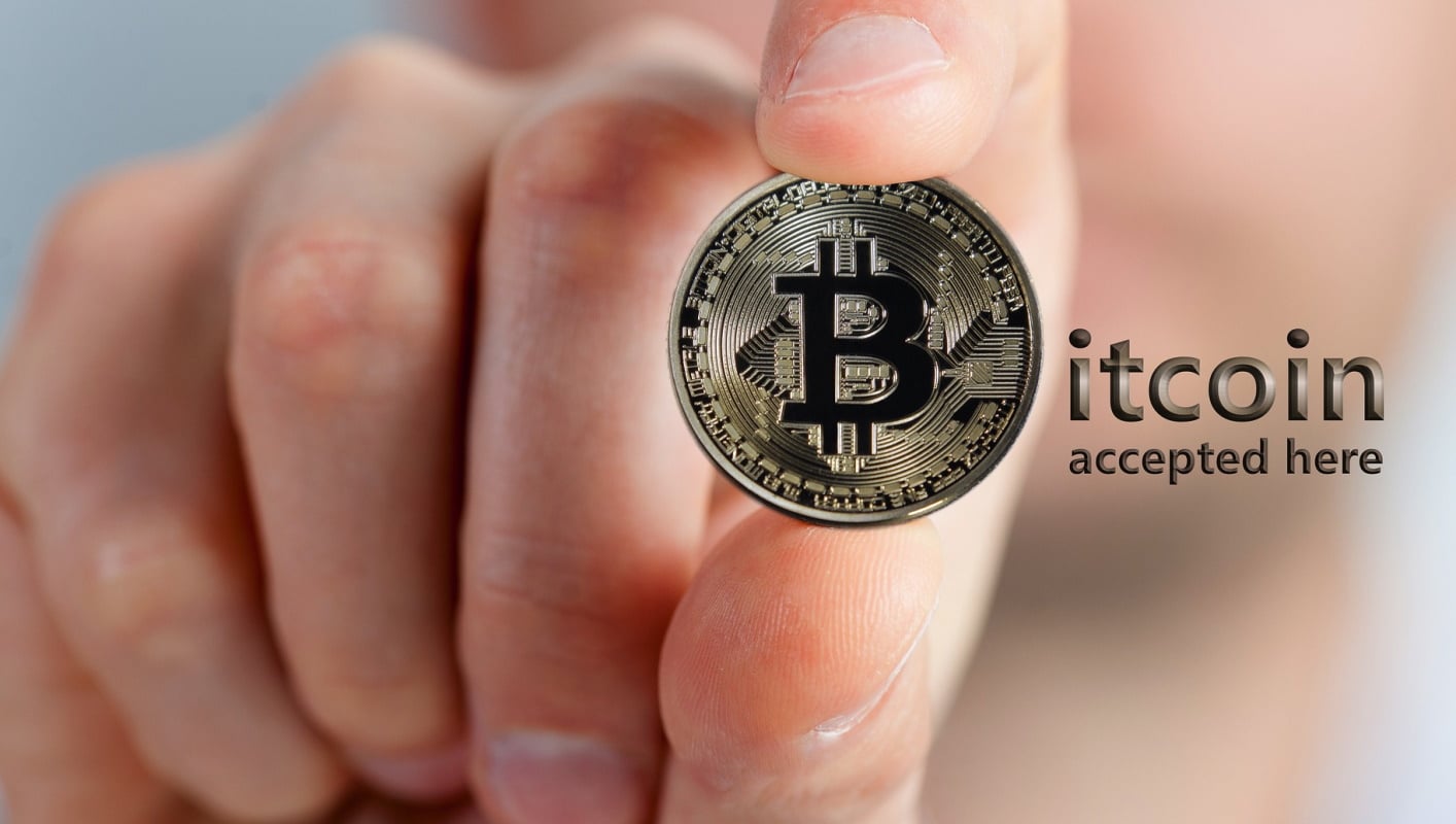 Imagem mostra mão segurando bitcoin e frase "aceitamos aqui" em inglês. PayPal anunciou que aceitará criptomoedas como forma de pagamento na plataforma