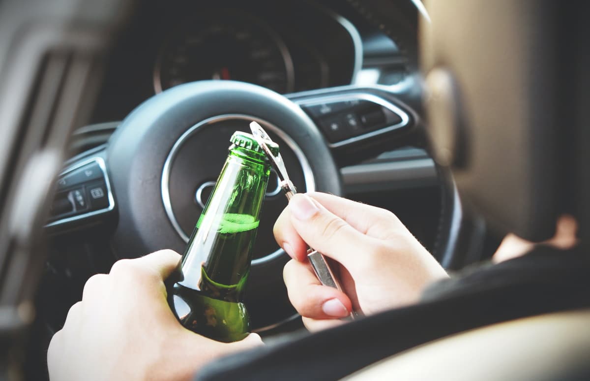 Imagem mostra motorista sentado no carro abrindo garrafa de cerveja