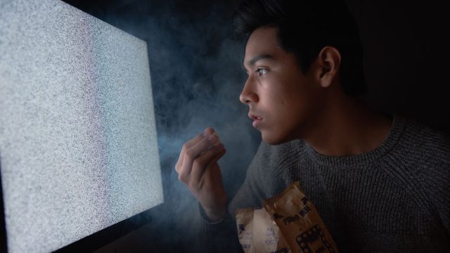 jovem assistindo tv fora do ar com pacote de pipoca em mãos