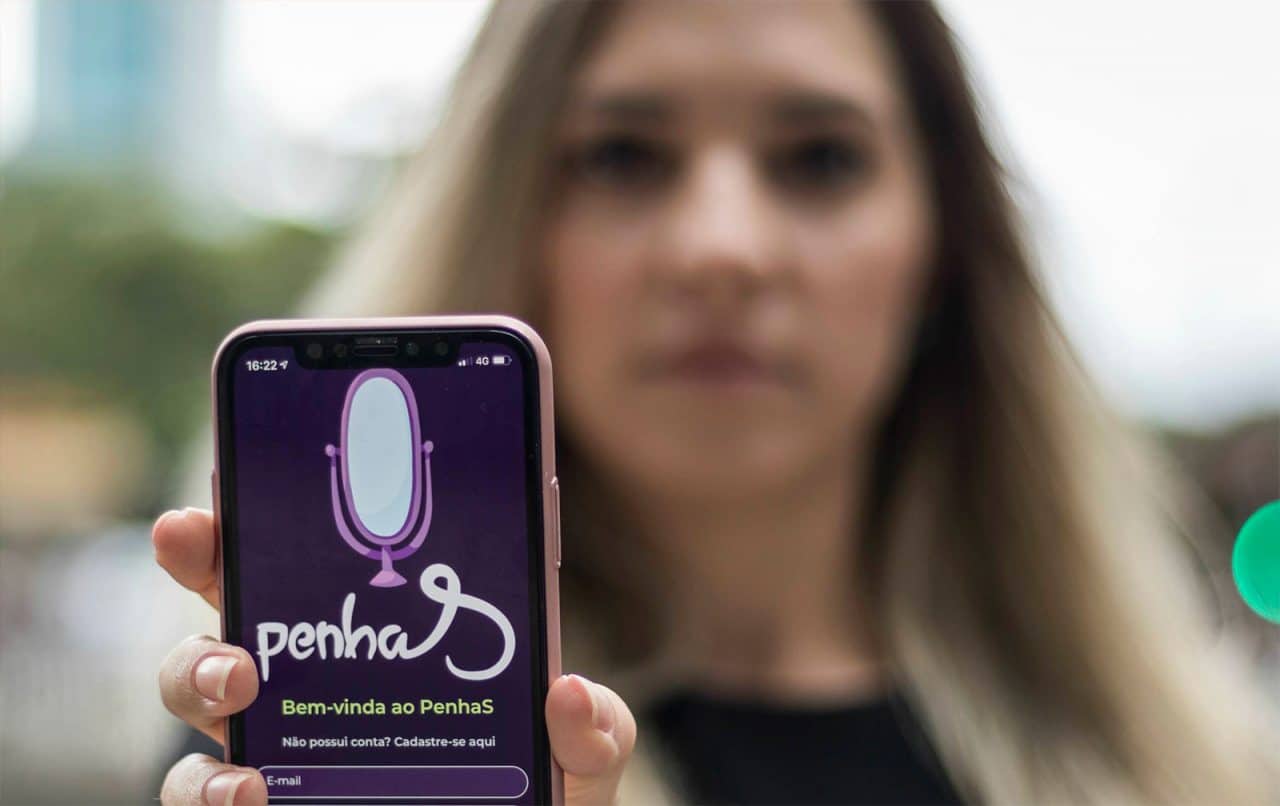 Imagem de um celular com o app PenhaS contra violência doméstica nas mãos de uma mulher