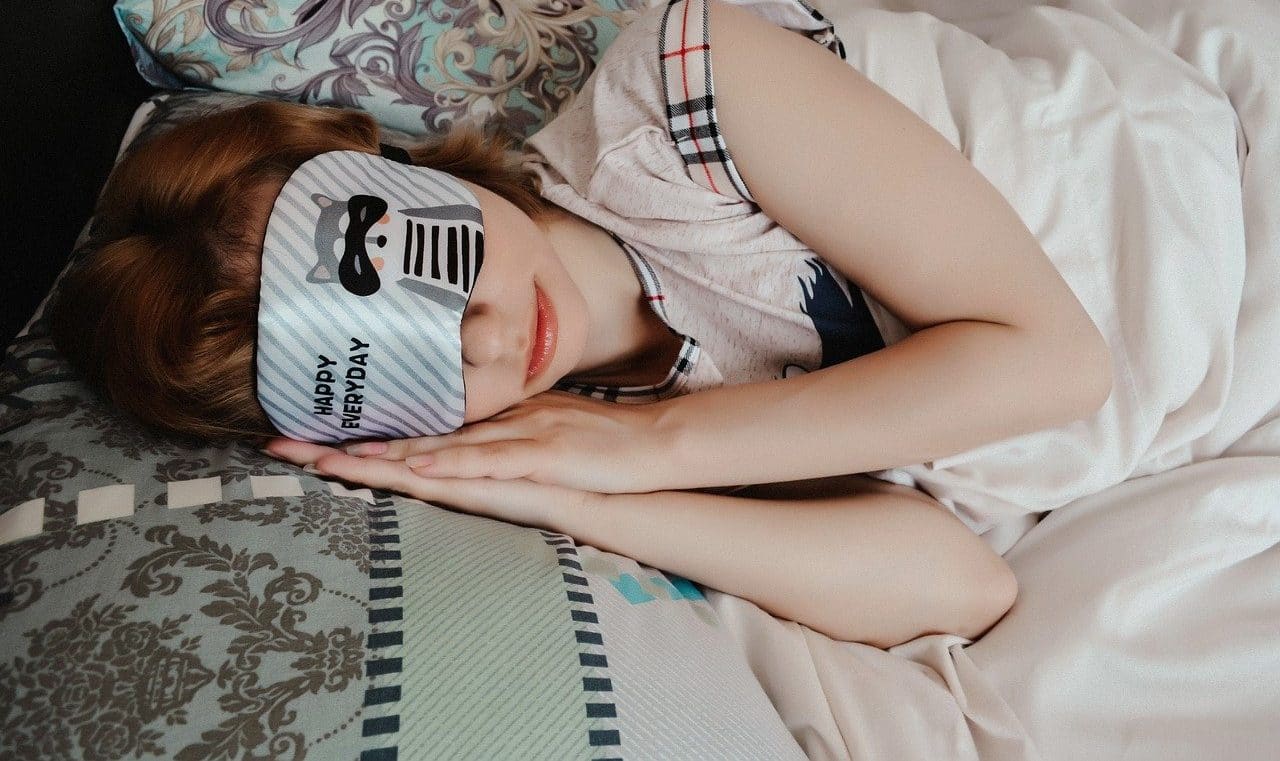 mulher usando uma máscara de sono e dormindo tranquilamente sobre um colchão