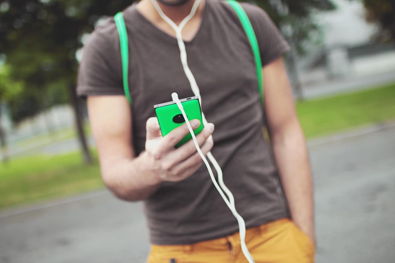 homem ouvindo áudio com um celular verde na mão