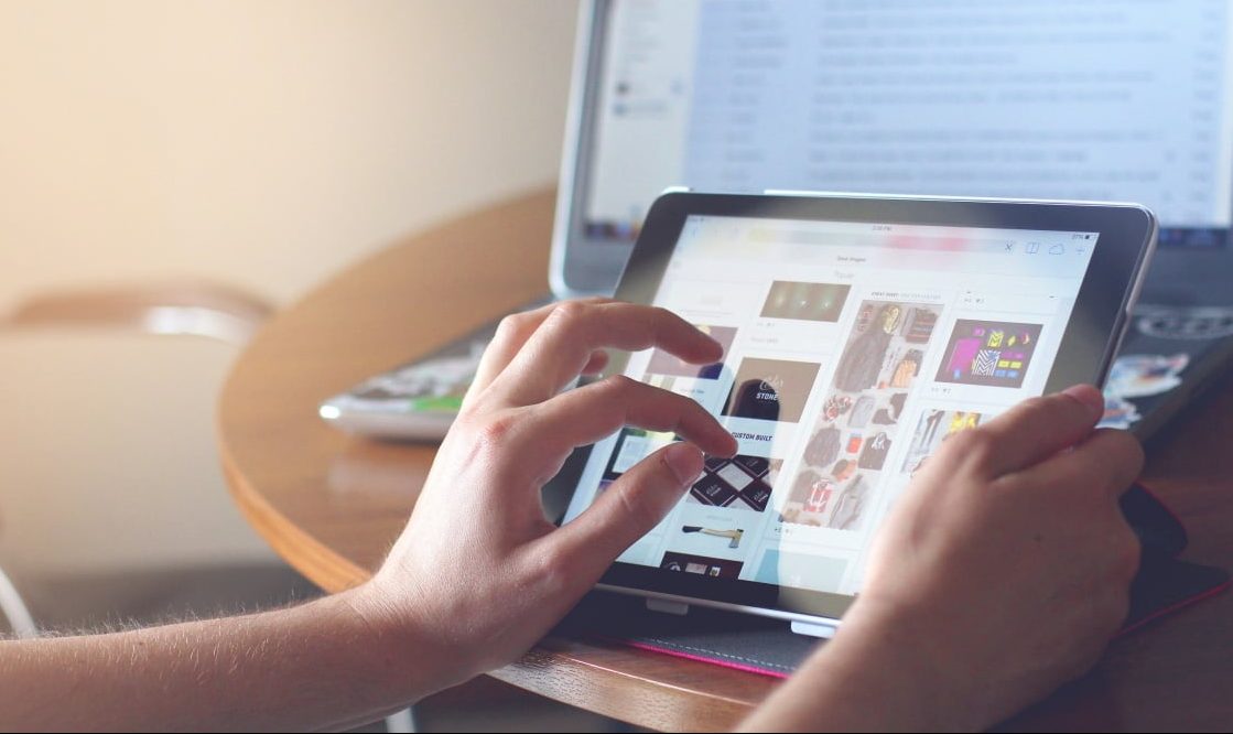 Imagem mostra mãos mexendo em um tablet, com monitor de um computador ao fundo. Lenovo pode mandar um tablet com sistema Android e o brand Yoga ao mercado em breve