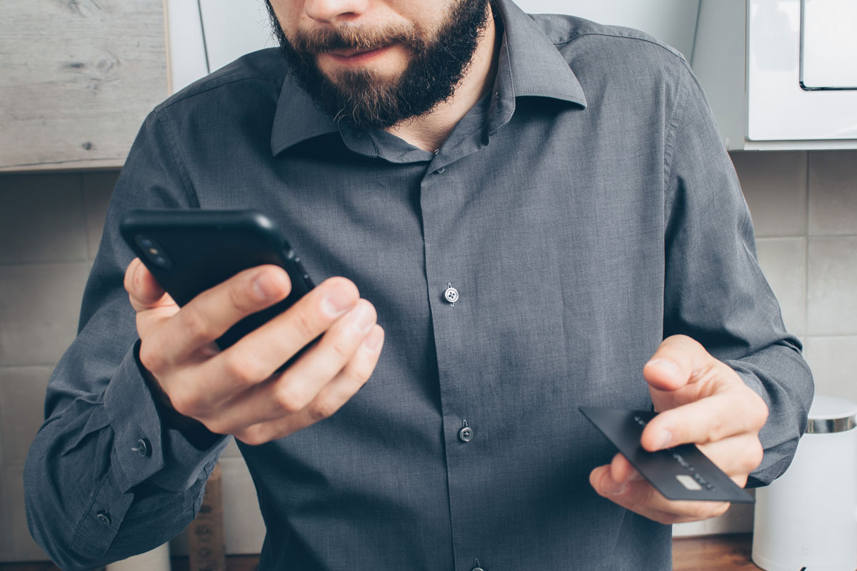 Homem preocupado segurando celular e cartão de crédito
