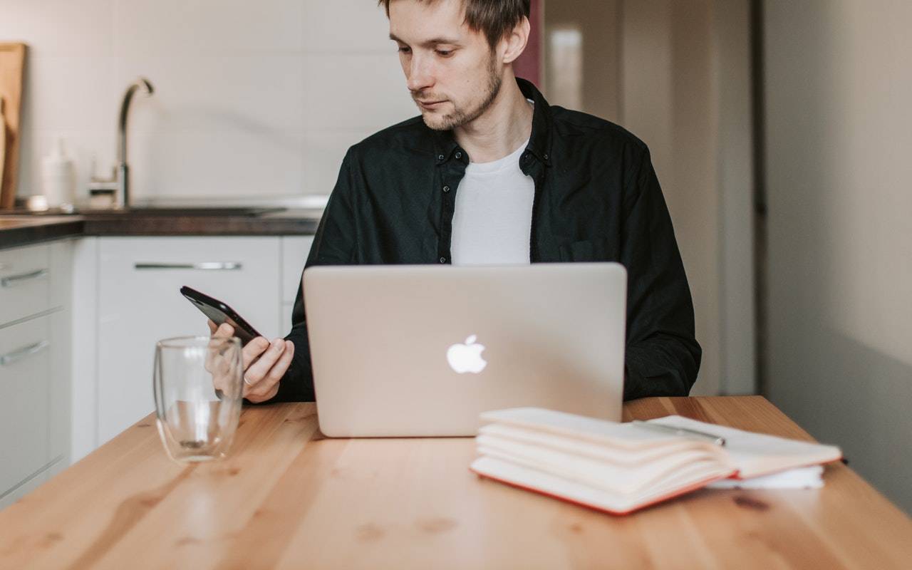 homem fazendo download de backups do WhatsApp no celular Android e mexendo em um computador com iOS