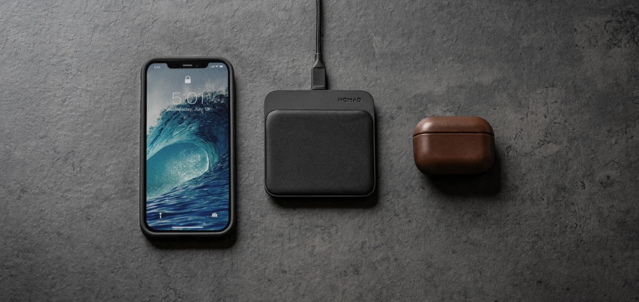 Base carregadora da Nomad ao lado de um iPhone e case de AirPods