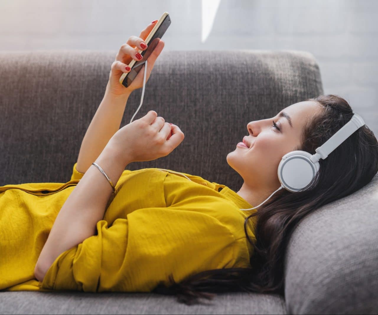 Mulher deitada no sofá ouvindo música com fones de ouvido