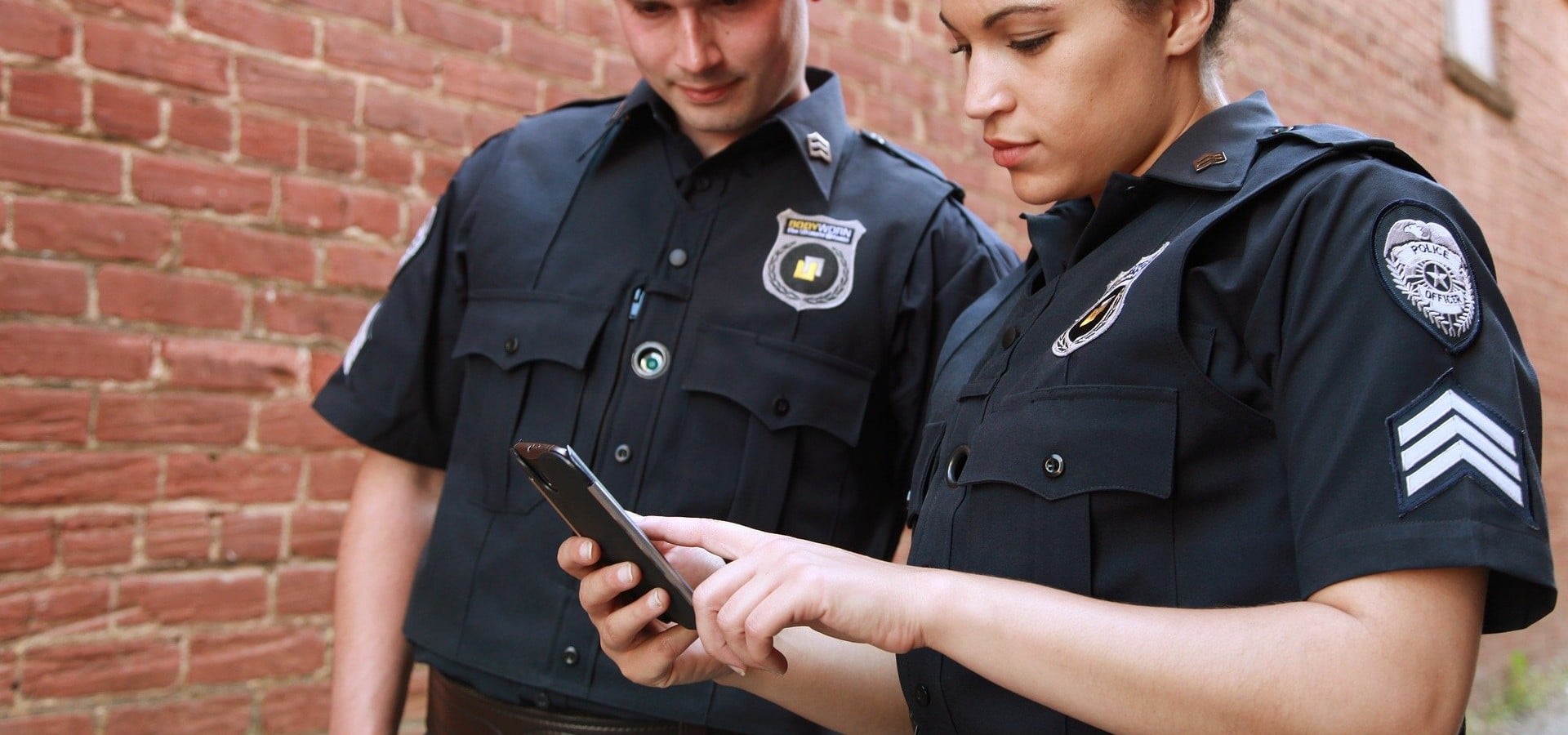 Policiais americanos inspecionando um celular para ilustrar o uso do gadget GrayKey pela polícia para desbloquear iPhones