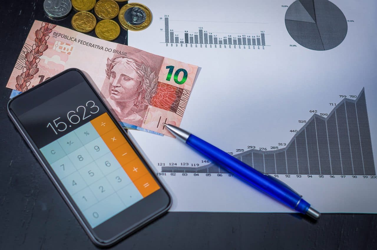 Imagem mostra celular com calculadora aberta, nota de 10 reais e caneta. Especialista explicou se é hora de trocar plano pré pelo pós do celular