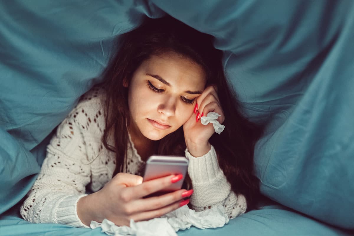 memina chorando na cama com smartphone na mão