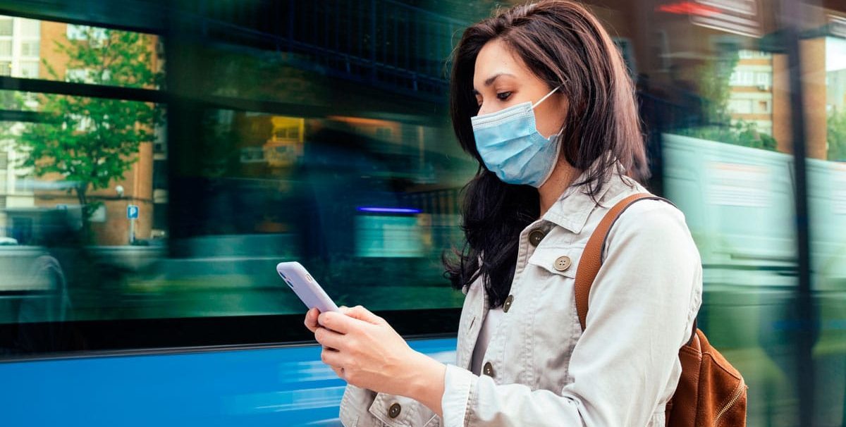 mulher de máscara mexendo no celular esperando no ponto de onibus