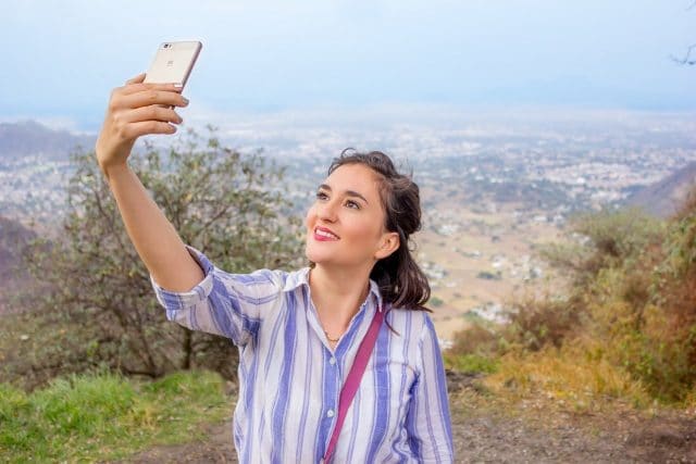 Imagem mostra mulher tirando selfie com paisagem ao fundo