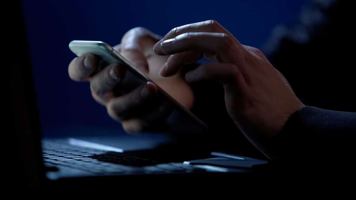 golpista usando celular na frente de laptop
