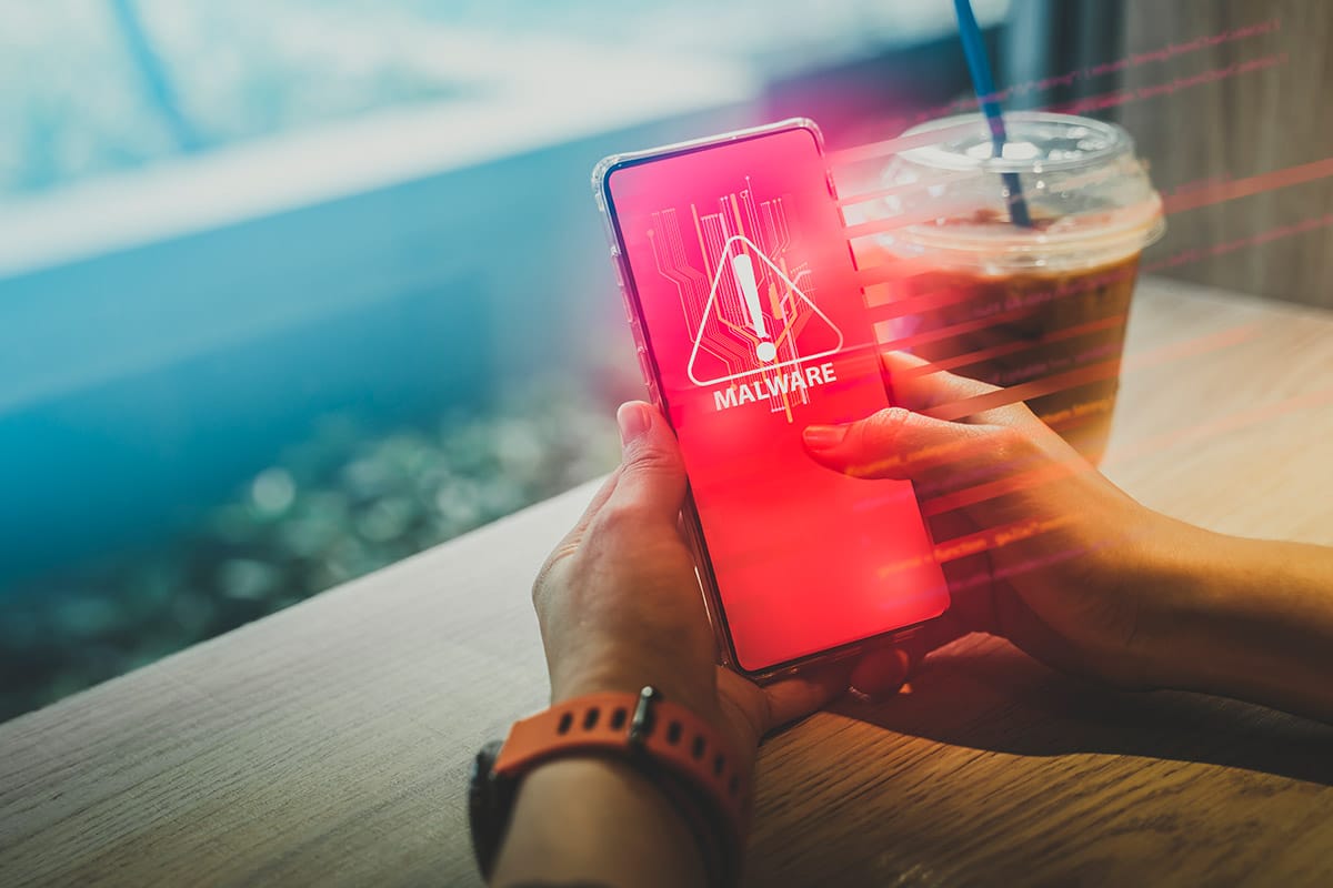 pessoa na mesa usando smartphone com malware e copo de milkshake no fundo