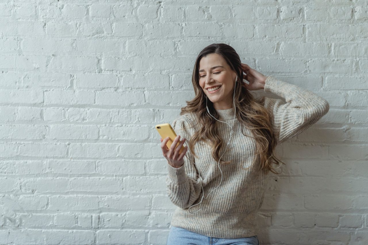 Imagem mostra uma mulher usando um celular de fones, possivelmente em uma chamada de vídeo