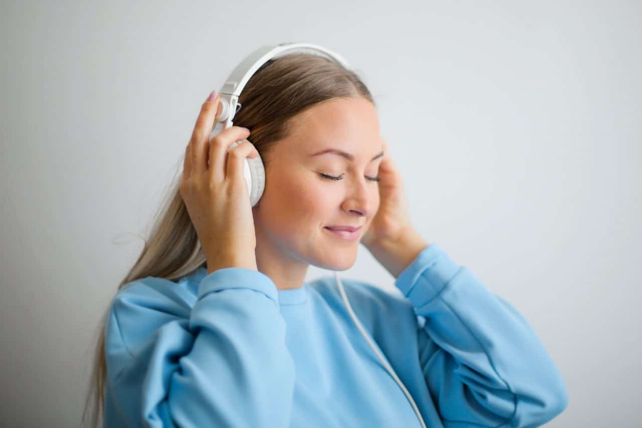 Imagem mostra uma mulher ouvindo música com fones brancos