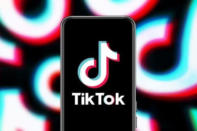 Foto com um celular usando o TikTok e o logo da empresa replicado como padrão ao fundo