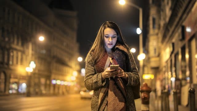 Mulher usando celular enquanto caminha em uma rua à noite