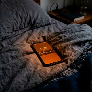 elular sobre uma cama no escuro, com a tela em tom alaranjado do modo noturno.