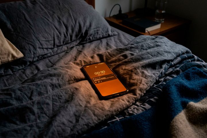 elular sobre uma cama no escuro, com a tela em tom alaranjado do modo noturno.