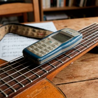 Celular Nokia antigo apoiado sobre um violão, com as cordas em primeiro plano.