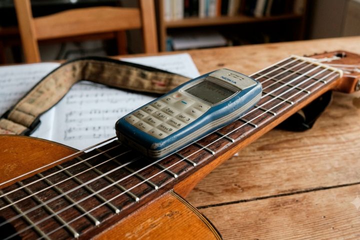 Celular Nokia antigo apoiado sobre um violão, com as cordas em primeiro plano.